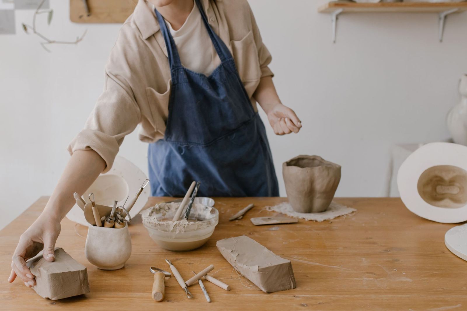 A maker shaping clay at a wooden workbench